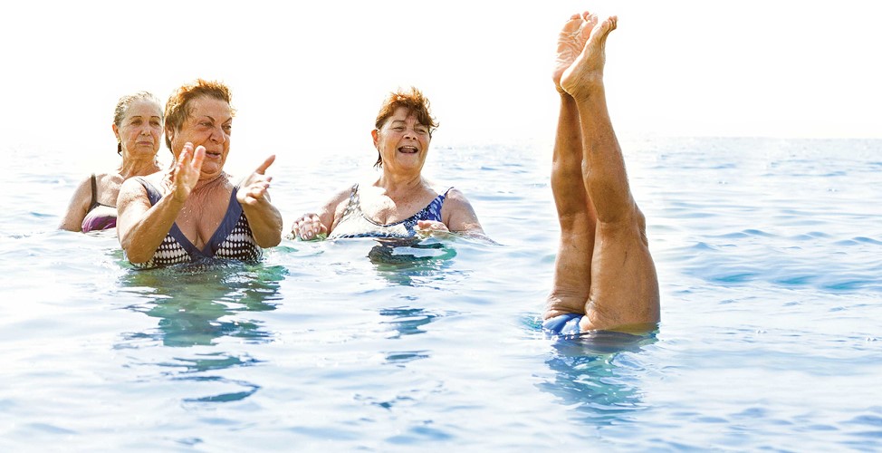 Older women in swimming pool doing water aerobics. One person is upside down with legs sticking out of the water.