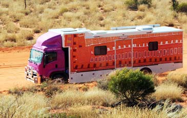 Truck driving through the outback with Aboriginal art painted on the carriage