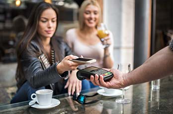 Female friends tapping card, paying for a coffee