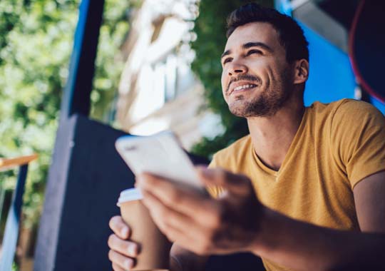 Man holding his mobile phone, sitting outside and smiling