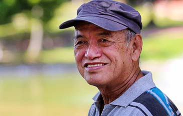 Older man smiling at camera with greenery in the background