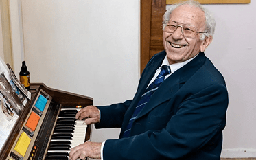 Person wearing glasses and a suit seated at an electronic piano keyboard indoors, with hands on the keys