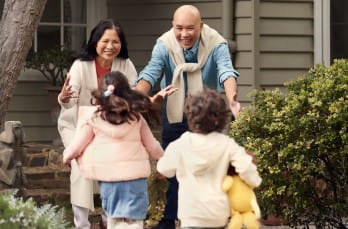 Two children towards a man and a woman outside a house