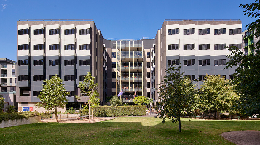 7 storey apartment building, with green grass and trees at the front