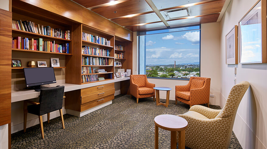 Library shelves full of book and desk with computer. 3 armchairs and coffee tables