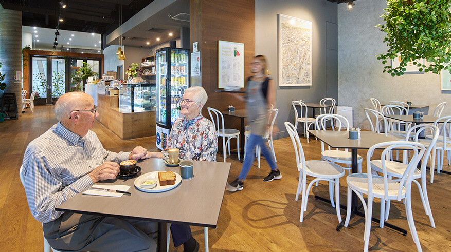 Cafe with 2 elderly people sitting on a table enjoying a meal.