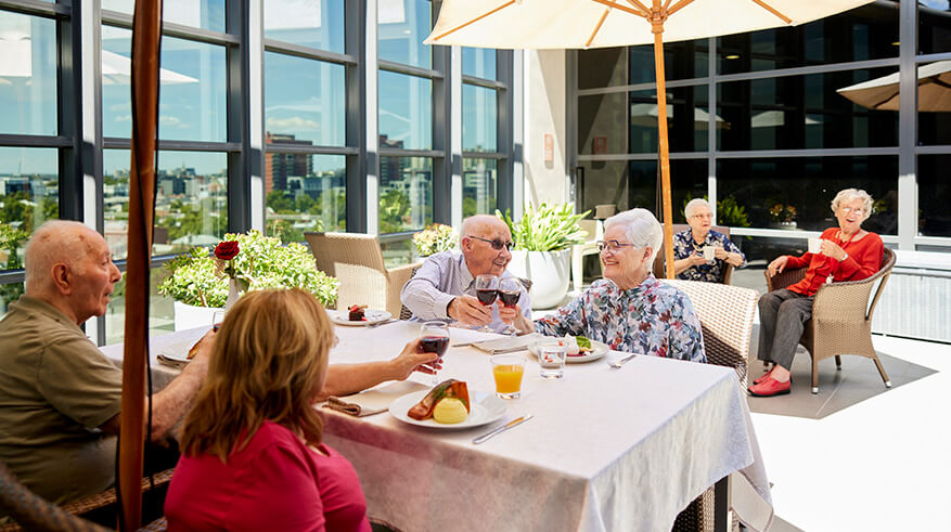 Residents sitting outside on the patio, eating at tables with cream umbrellas out for shade.