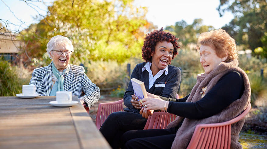 Residents and staff laughing and enjoying a conversation outside on an Autumn day