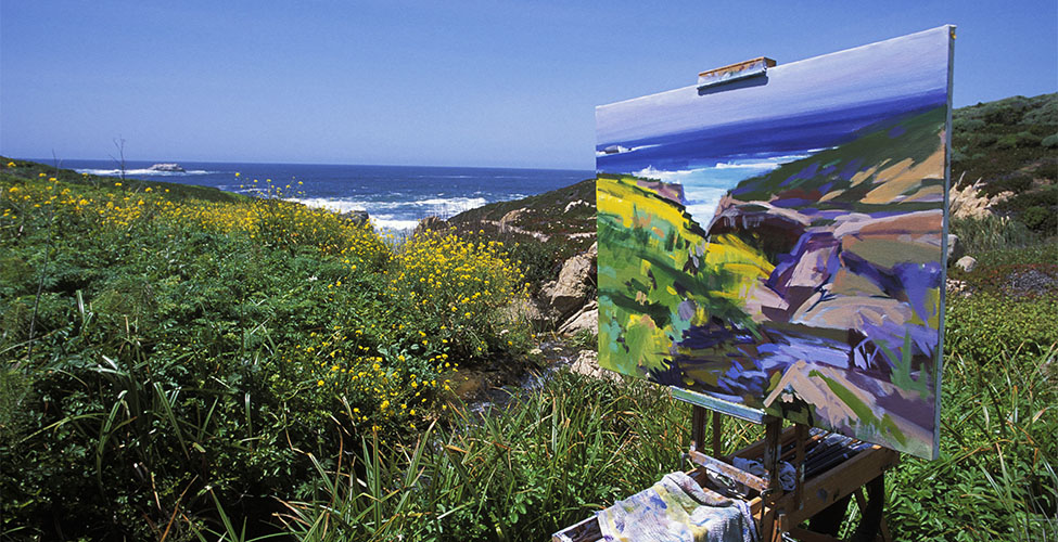 An awe-inspiring landscape of plants and the ocean, with someone's painting of it in the foreground