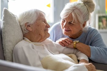 An older woman in a hospital bed smiles warmly at her family.
