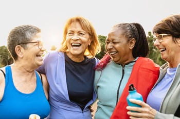 A group of retirees laughing and hugging on the beach after pilates. 