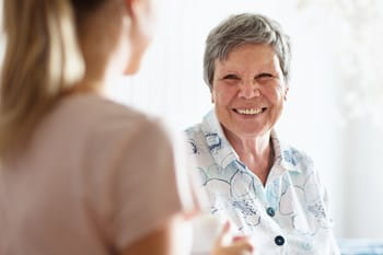 A retiree smiles brightly at a nurse off camera.