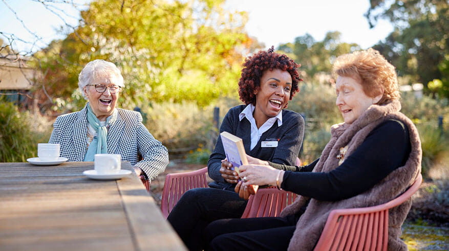 Residents and staff laughing and enjoying a conversation outside on an Autumn day