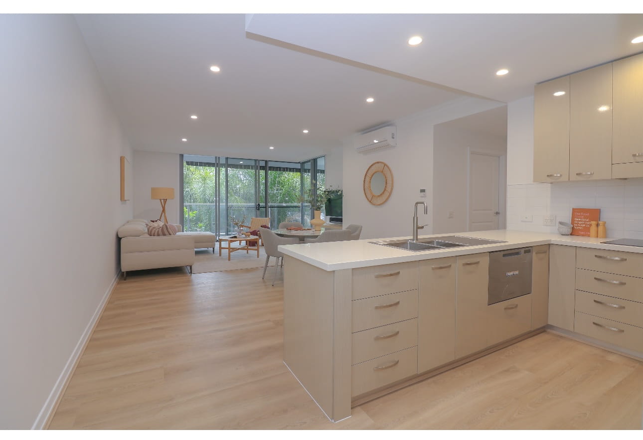 Modern open-concept living area with a beige kitchen, island, and light wood floors.