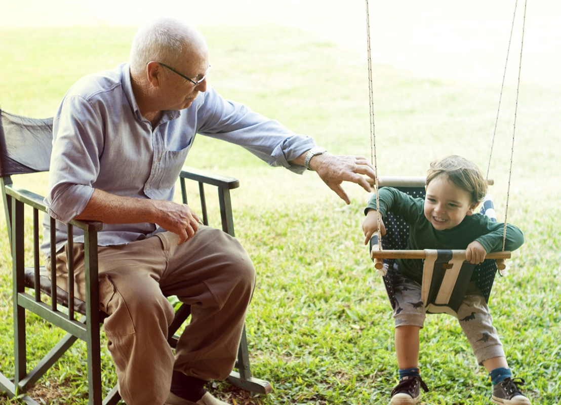 Image of a Grandfather figure pushing grandson on a swing