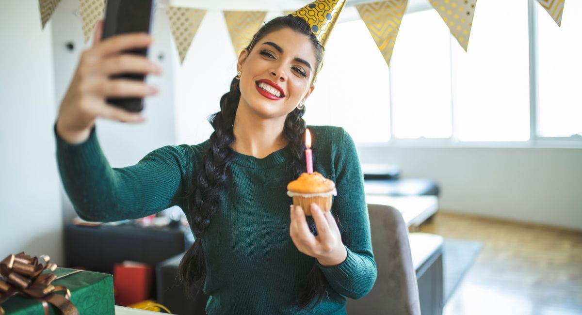 A woman in an empty apartment taking a selfie with a birthday cupcake.