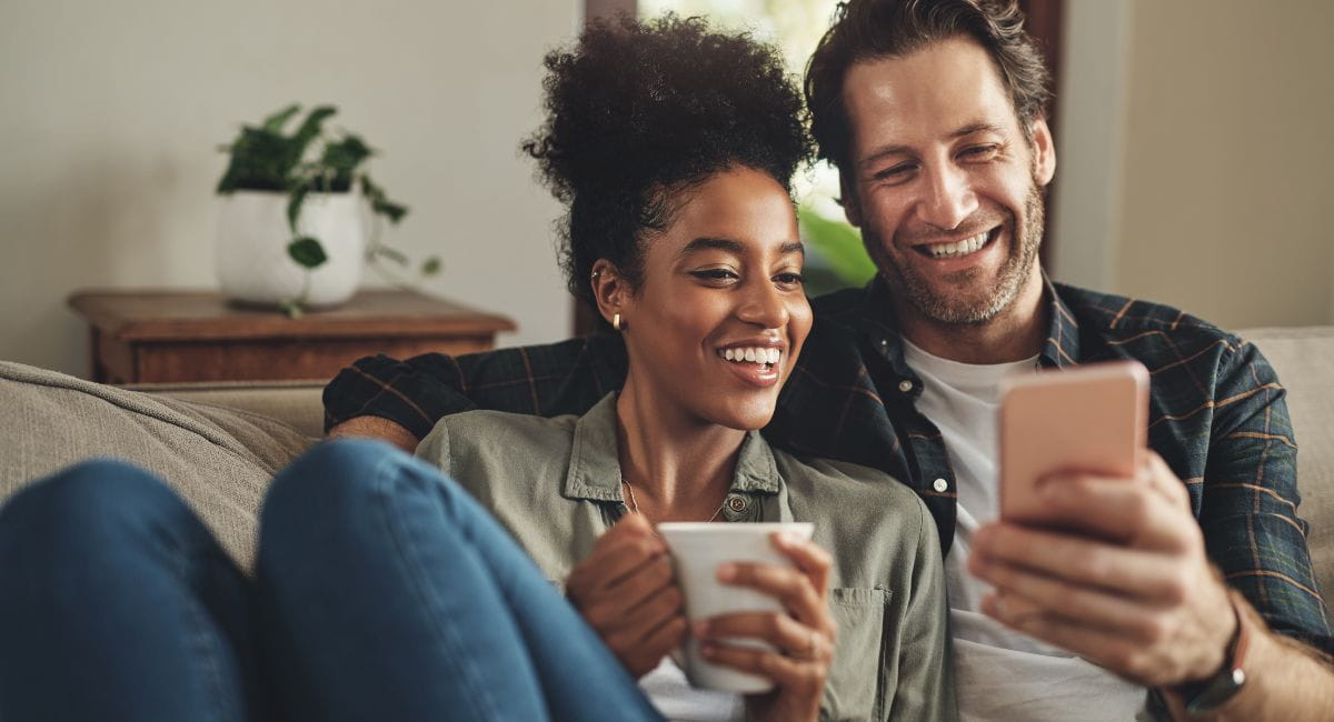 A young couple lounging on the couch and smiling at eachother.