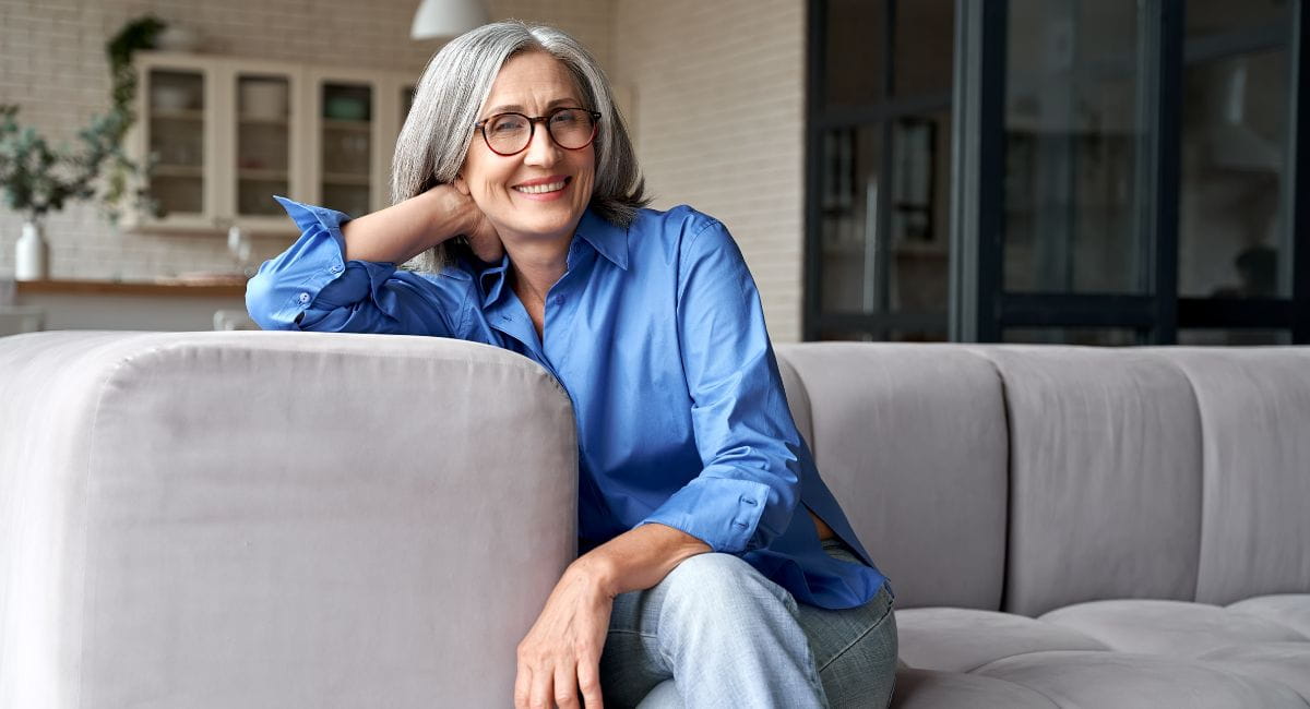 An older woman smiling while lounging professionally on a counch.