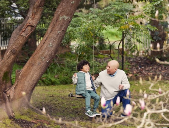 A man kneeling down next to a child on a rope swing
