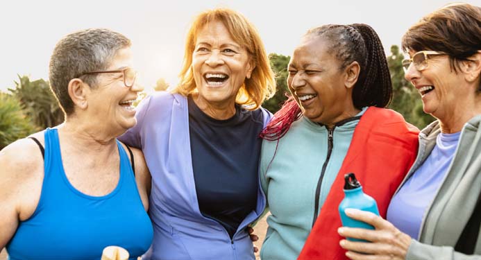 Four women in exercise clothes, hugging and smiling