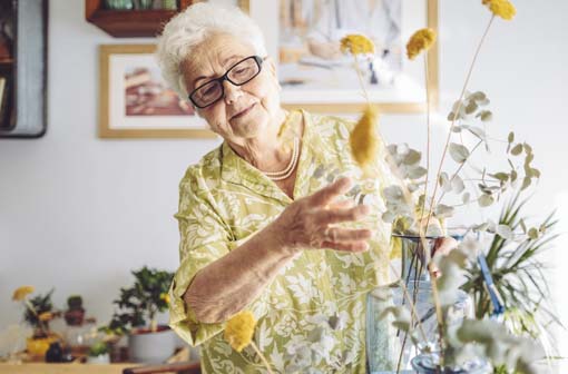 Elderly woman putting flowers into a vase with a smile on her face