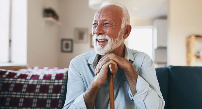 Elderly man sitting on a couch laughing, leaning on a walking stick