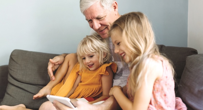 Grandfather sitting on couch with two grandchildren, looking at the phone smiling