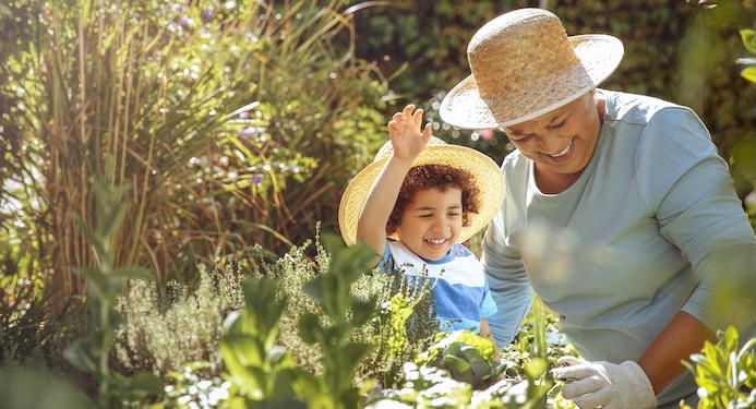 Grandmother in garden with grandchild with gardening gloves and sun hats on