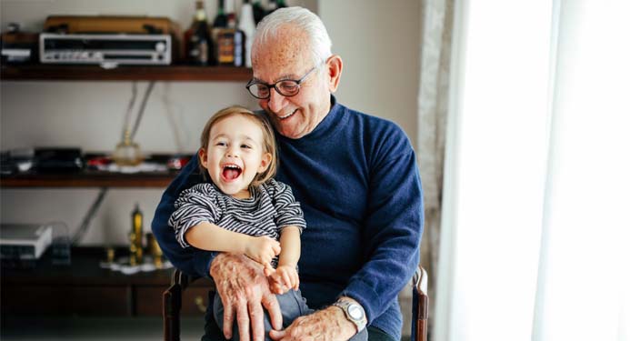 Grandfather holding his grandchild while sitting down, both smiling and happy