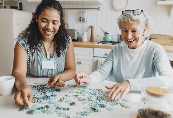 Care worker and woman solving a puzzle in the kitchen, smiling