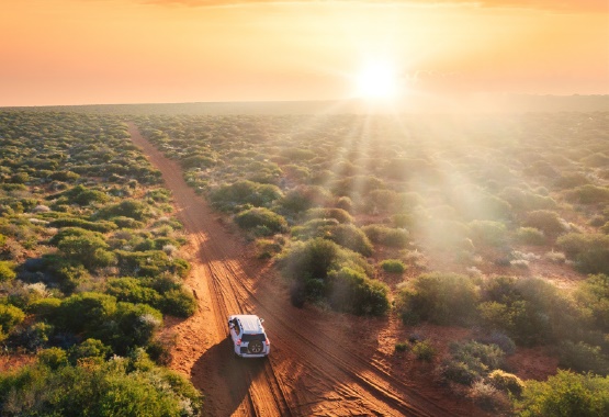 A white SUV driving along a dirt road in the outback at sunset