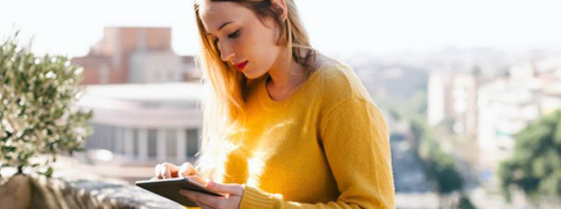 A young woman on a balcony looking at a tablet