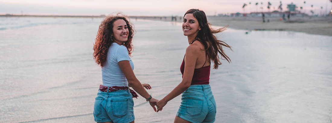 Two young woman holding hands and walking along the beach