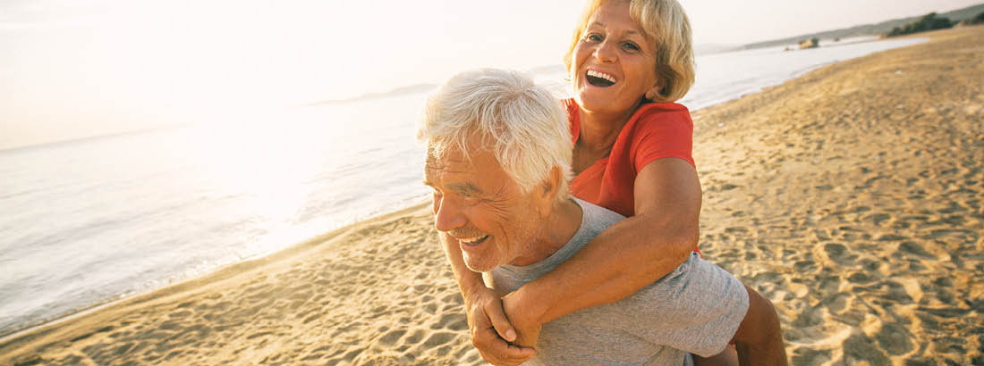 An older couple of the beach with the man piggybacking a woman