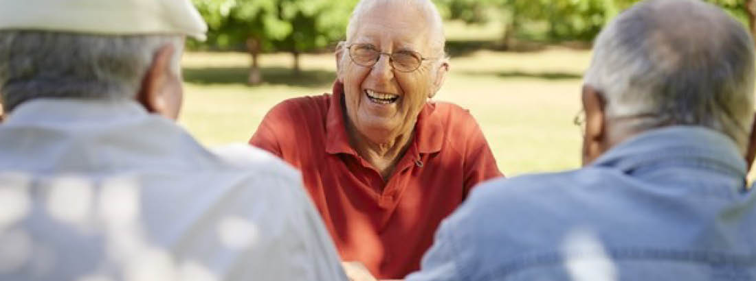 Three older men sitting together and one of the older men is laughing