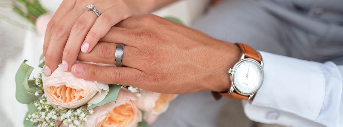 A wedding photo of a woman's hand over the man's hand showing their rings
