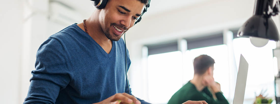 A young man sitting at a desk with headphones and working