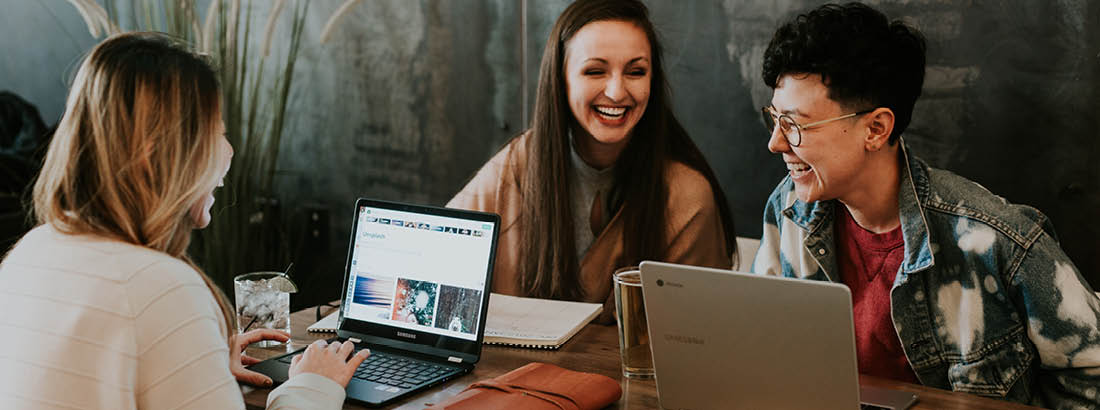 Three woman sitting at a cafe working on laptops and laughing