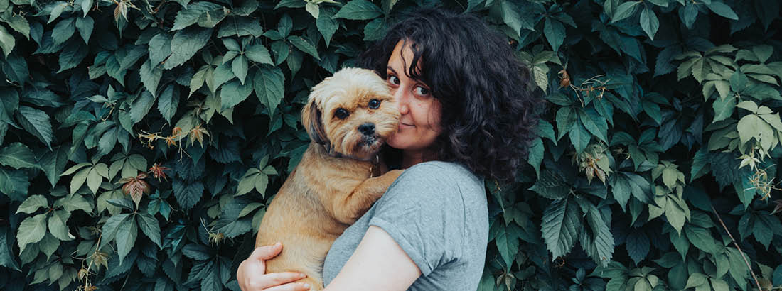 A young woman cuddling her dog in front of a tree