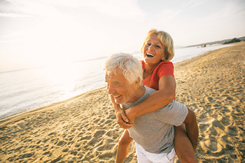 An older couple of the beach with the man piggybacking a woman