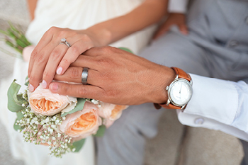 A wedding photo of a woman's hand over the man's hand showing their rings