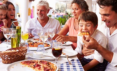 Multi-generational family sitting at a table enjoying a pizza and wine