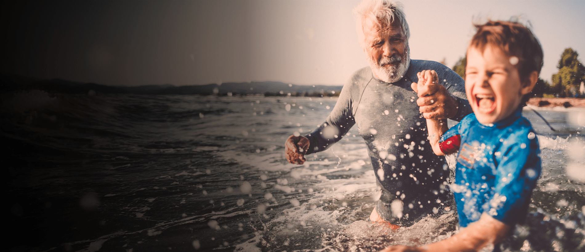 A father and son entering the surf on a sunny day.