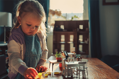 A child is playing with a dolls while the dollhouse standing in background.