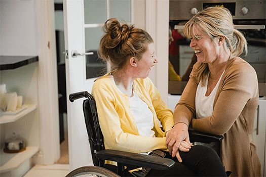 Mature mother is relaxing in the kitchen with her daughter who is in a wheelchair