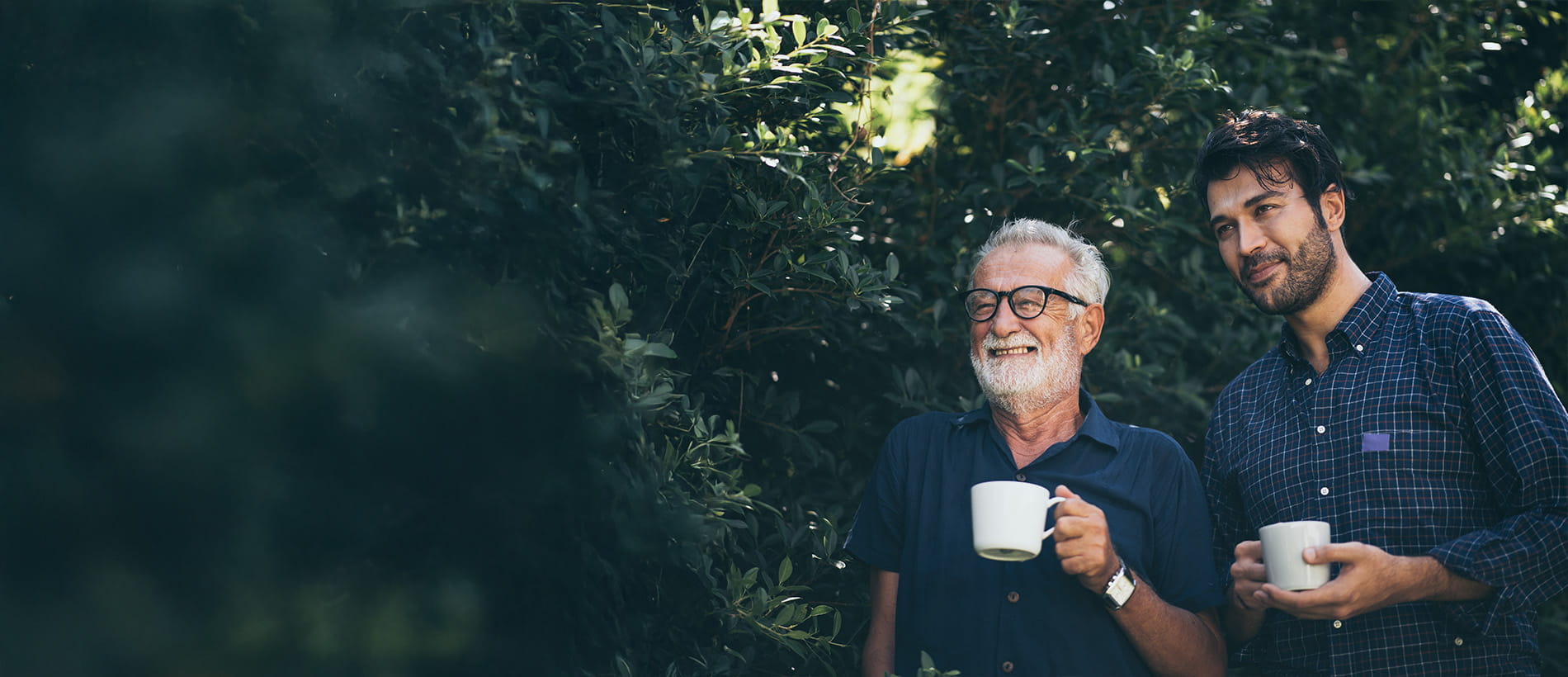 A father and son having a cup of tea in front of a bush