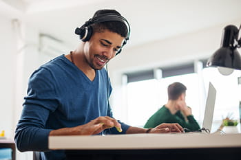 A young man sitting at a desk with headphones and working