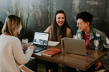 Three woman sitting at a cafe working on laptops and laughing