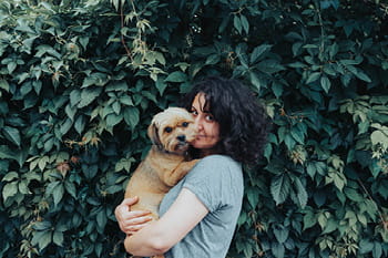 A young woman cuddling her dog in front of a tree