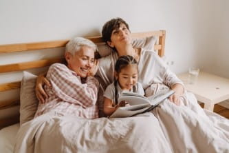 A grandmother, mother and a daughter sitting in bed reading